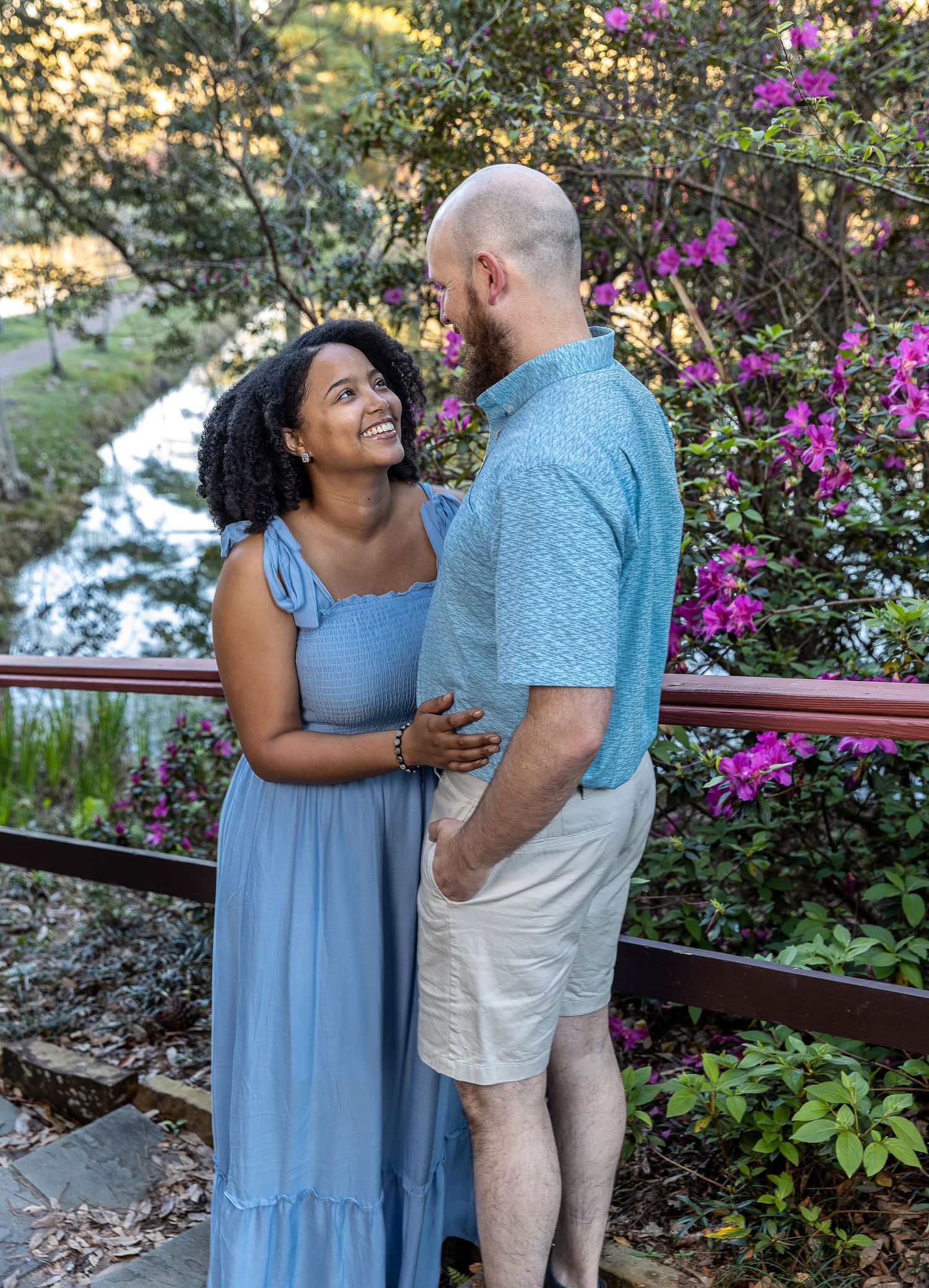 Happy couple sharing a moment outdoors with purple flowering bushes in background.