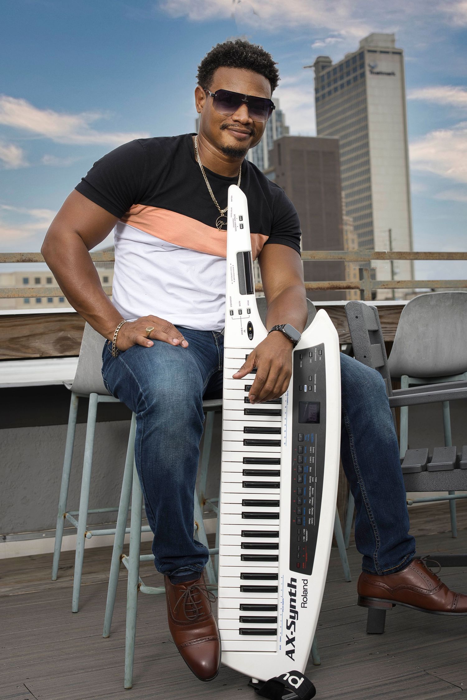 A musician poses with a white keyboard instrument on a rooftop terrace.