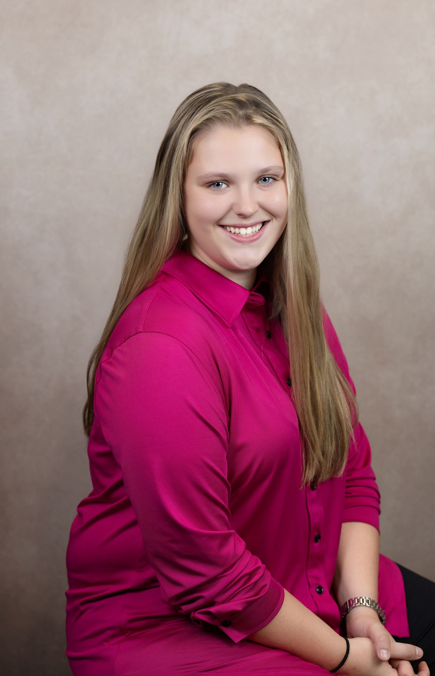 Portrait of a person wearing a vibrant pink button-up top and smiling warmly against a neutral backdrop.