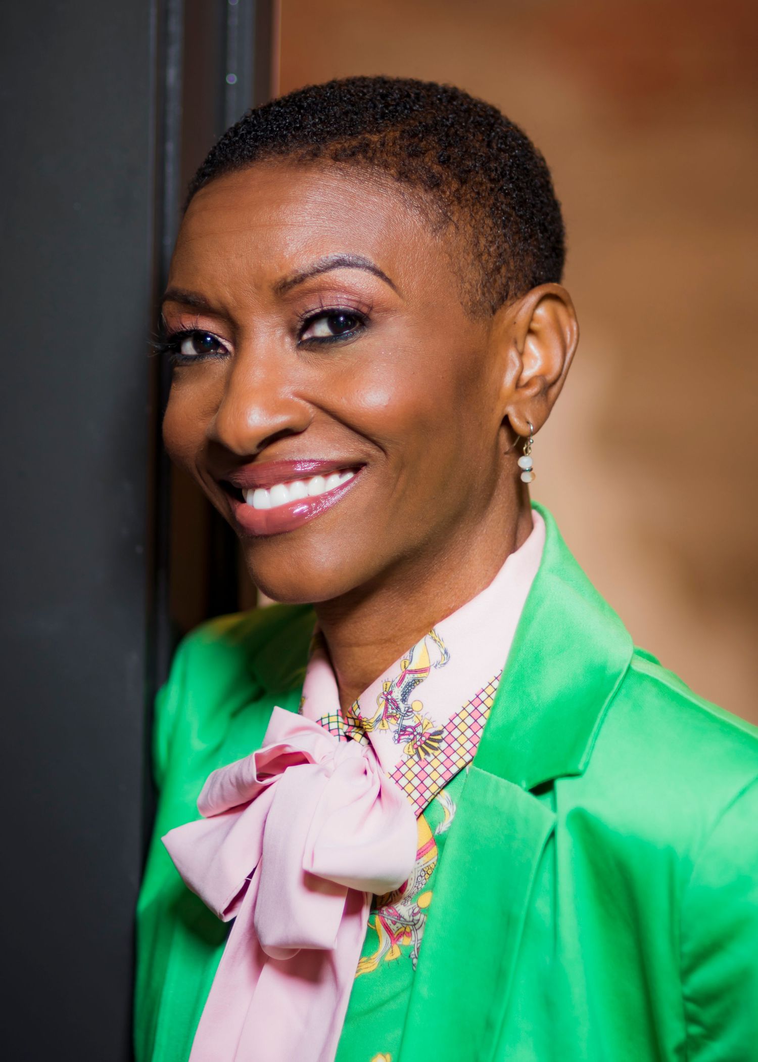 Professional wearing vibrant green blazer and pink bow tie smiles brightly.