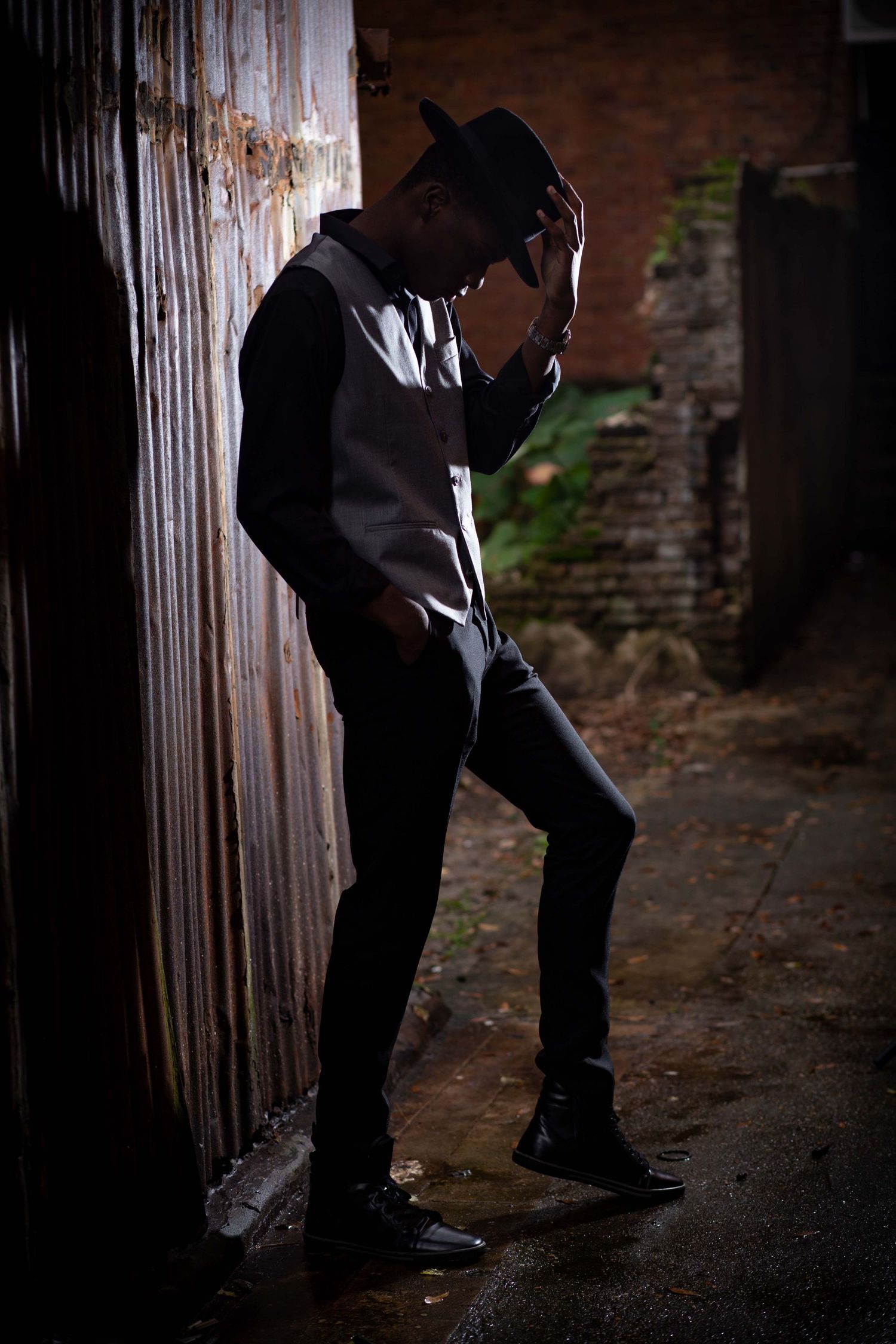 Dramatic silhouette of person in hat leaning against weathered wall.