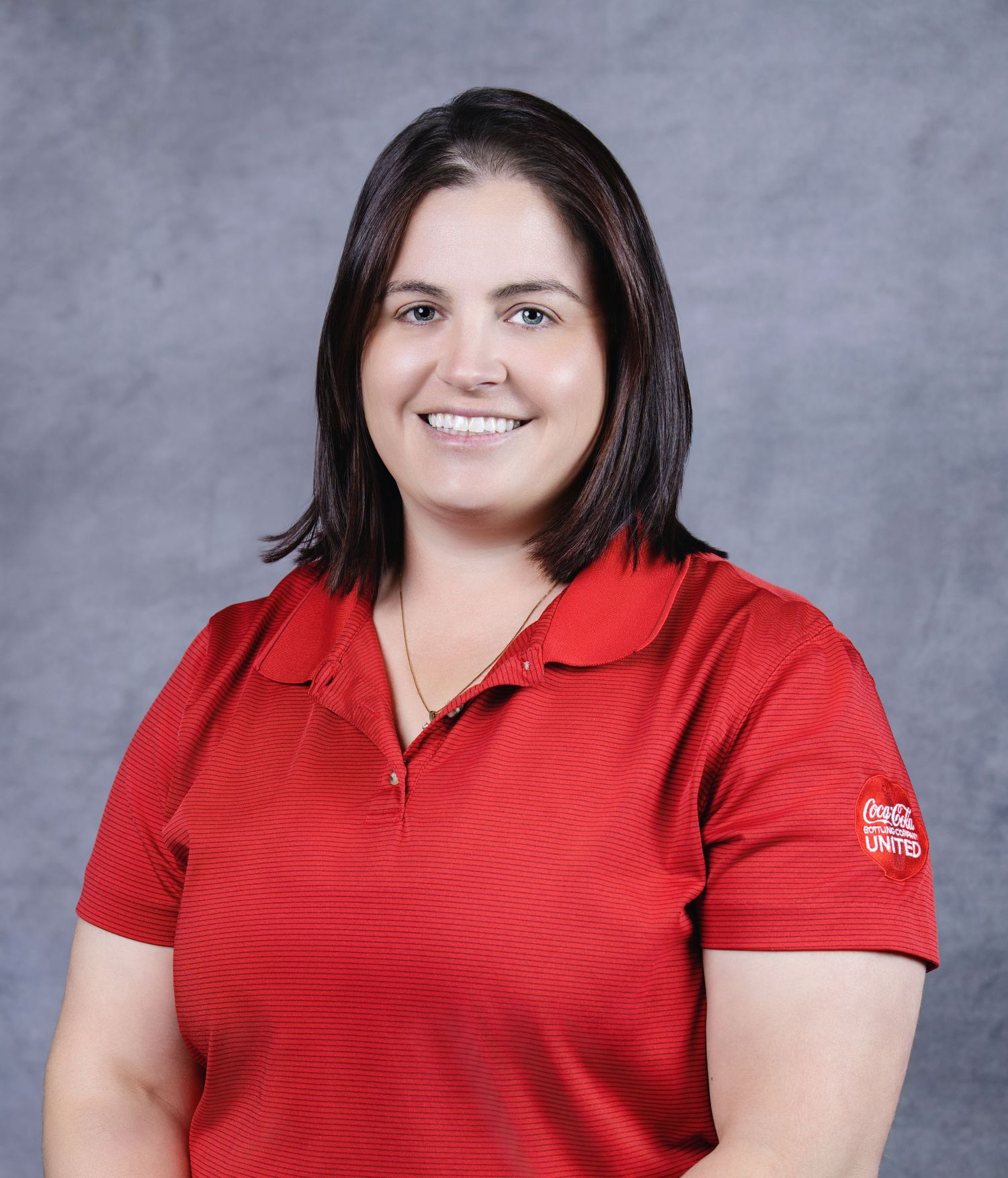 Professional headshot of someone wearing a red polo shirt against a grey studio background.