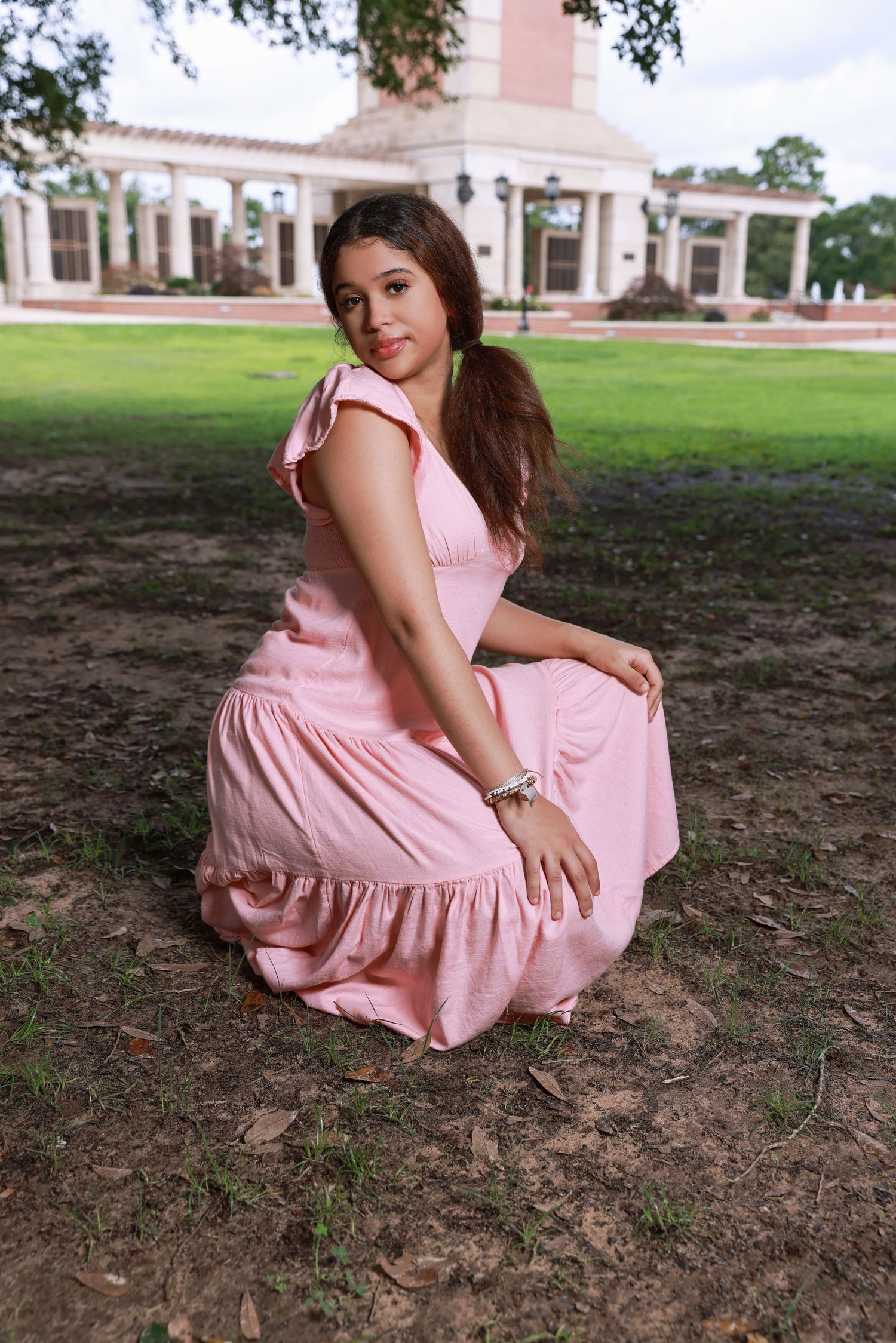 Woman in pink ruffled dress poses outdoors in front of classical white columned building.