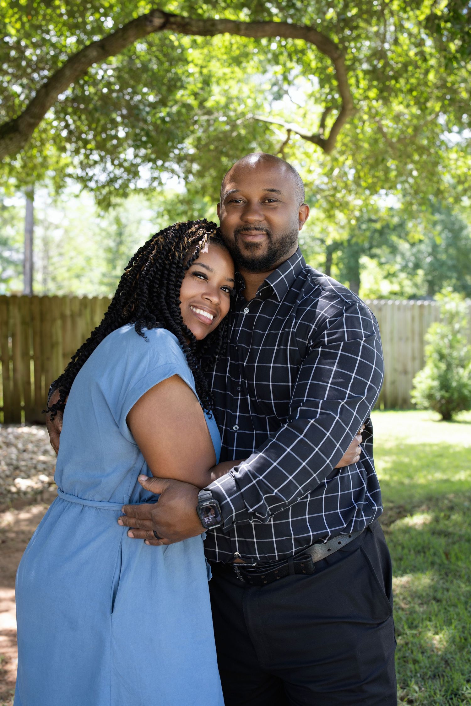 A loving couple embraces outdoors in a backyard setting with trees in the background.
