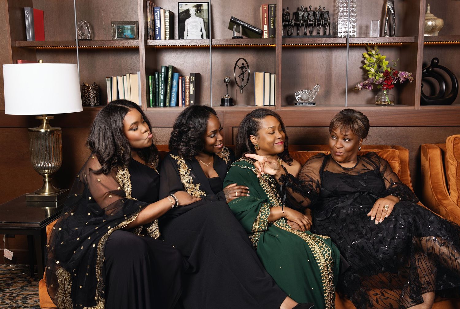 A group of people laugh and socialize while sitting on couches in a cozy living room with bookshelves.