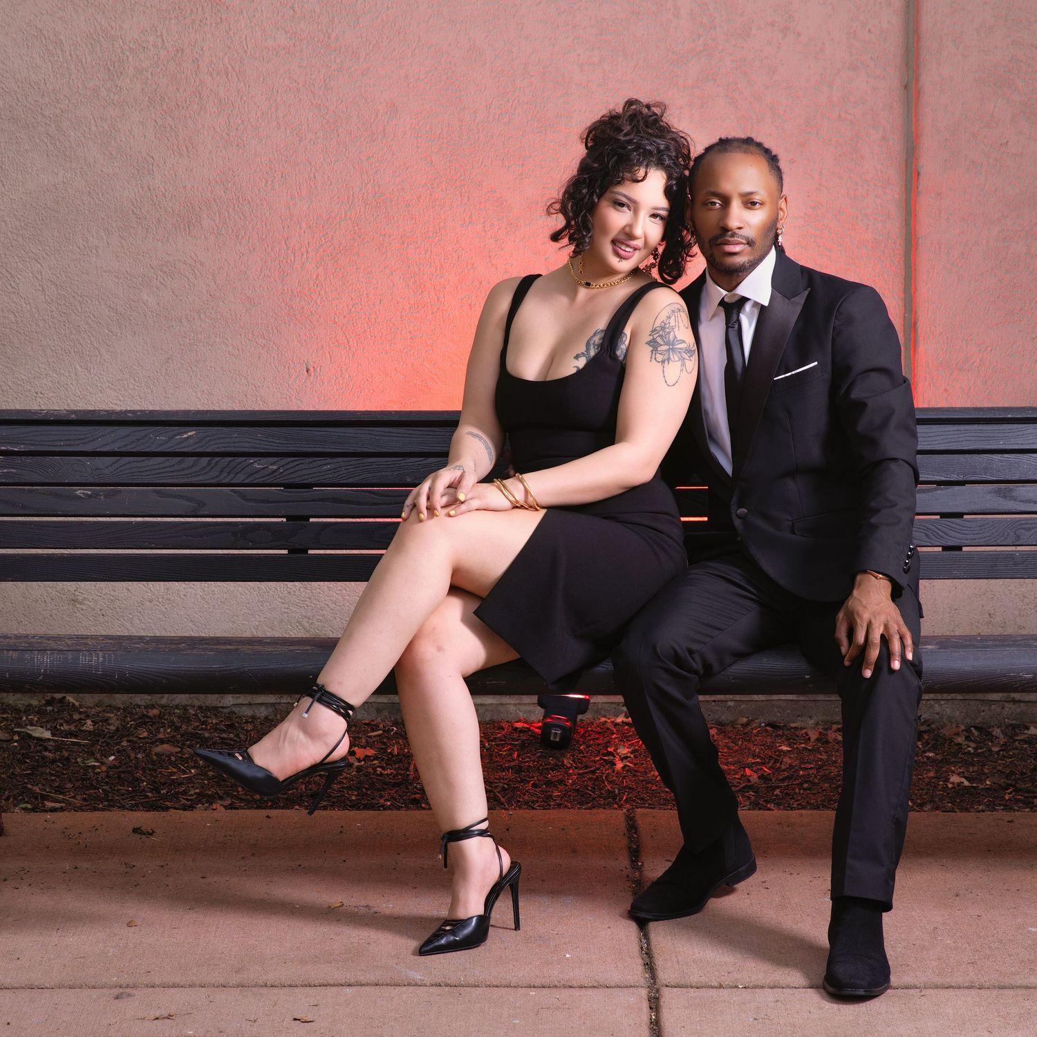 Elegant couple in formal attire sitting together on outdoor bench at night.