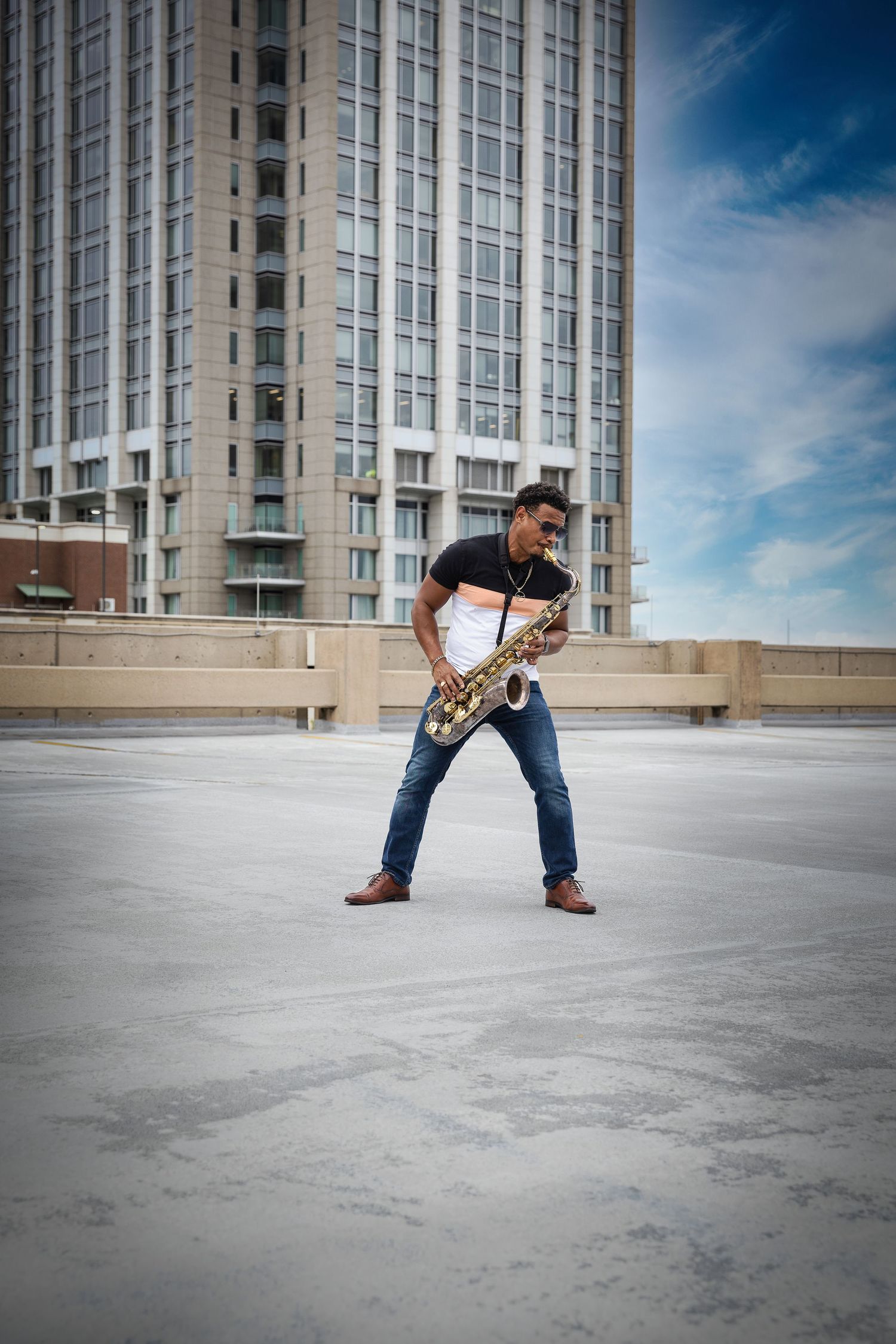 A musician plays a saxophone against a modern high-rise building backdrop on a rooftop.