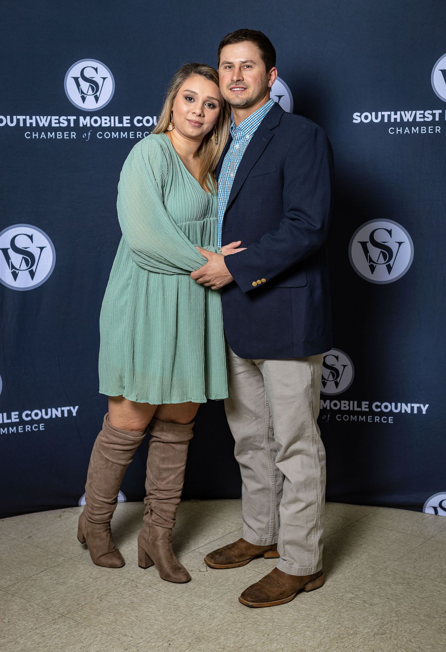 Couple posing at Southwest Mobile Chamber of Commerce event against branded backdrop.