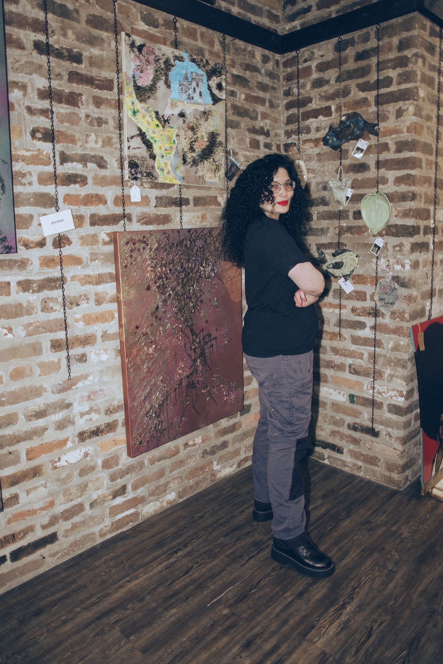 Artist standing near artwork on exposed brick walls in indoor setting.