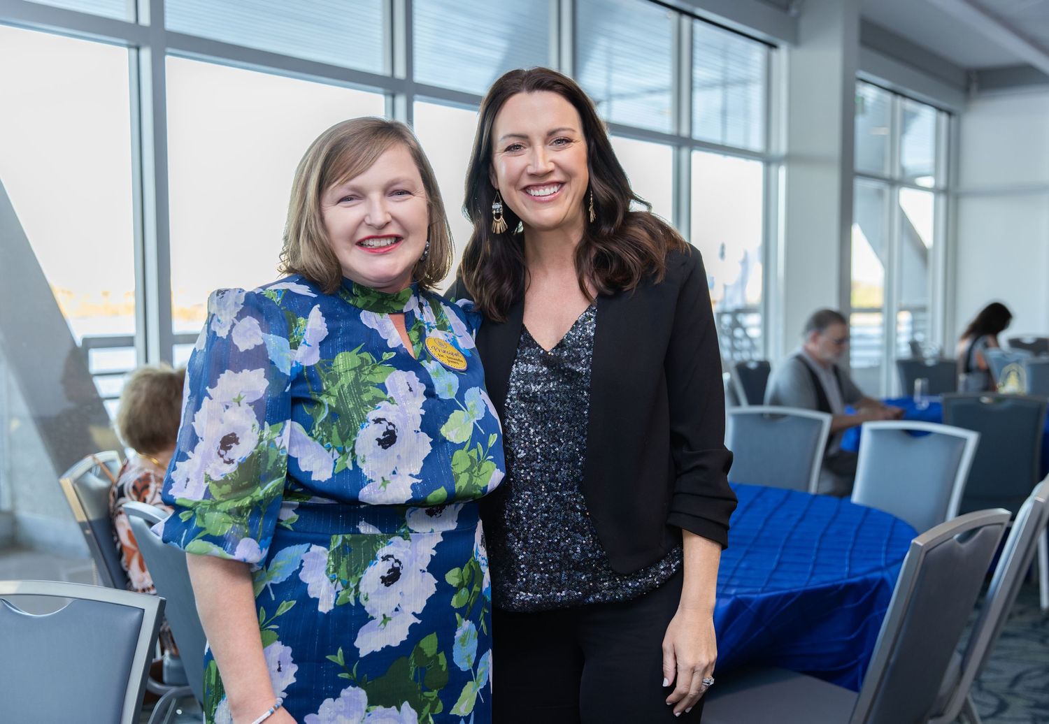 Three women in business attire smile together in a bright modern office space.