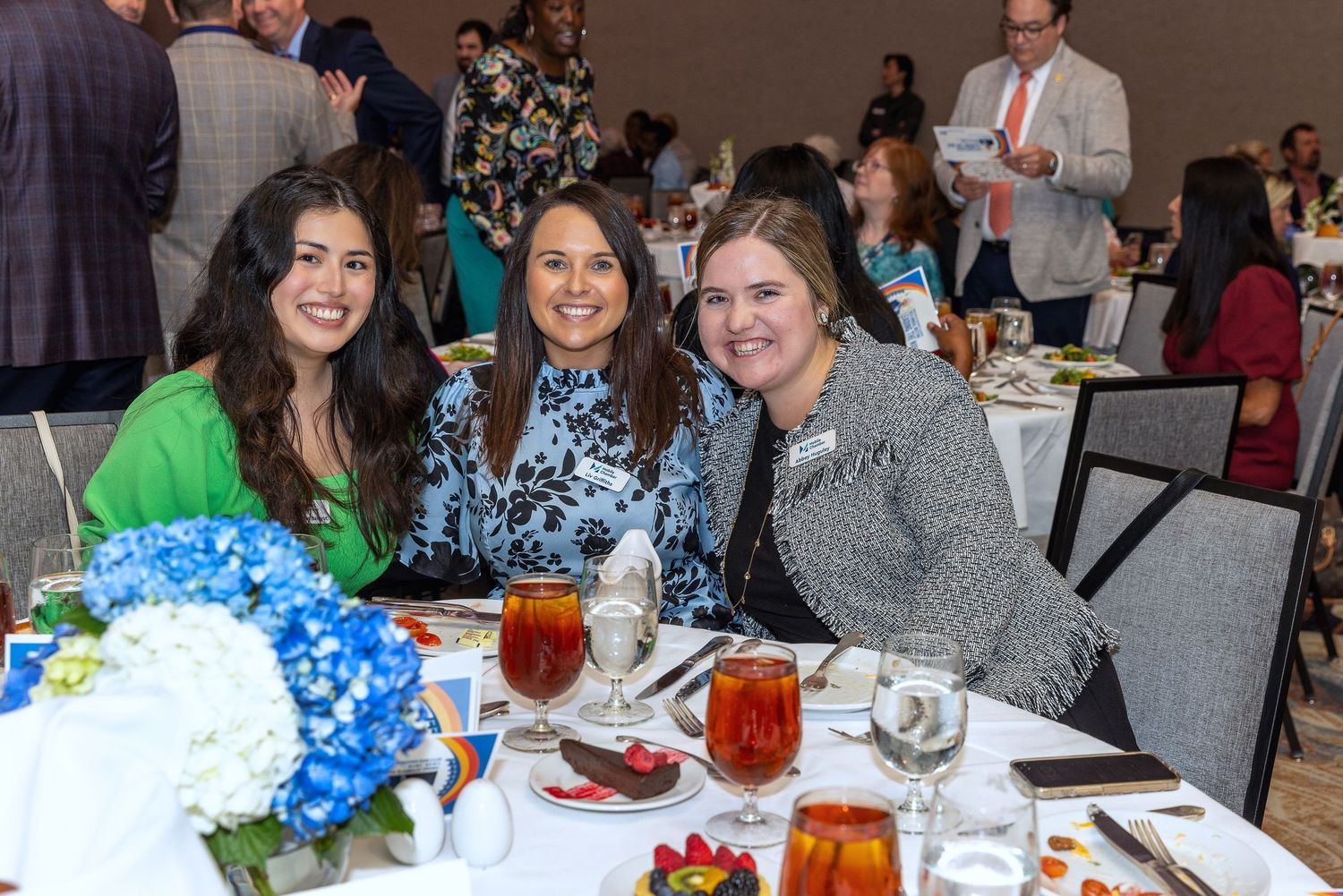 Three people smiling at dining table with blue hydrangea centerpiece.