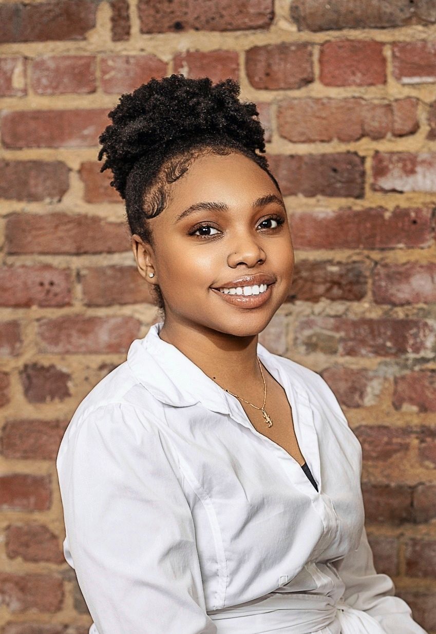 Professional portrait against brick wall featuring person in white top with natural hair styled up.