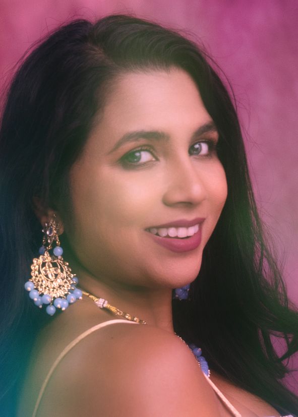 A glamour portrait features elegant jewelry and a soft smile against a pink background.