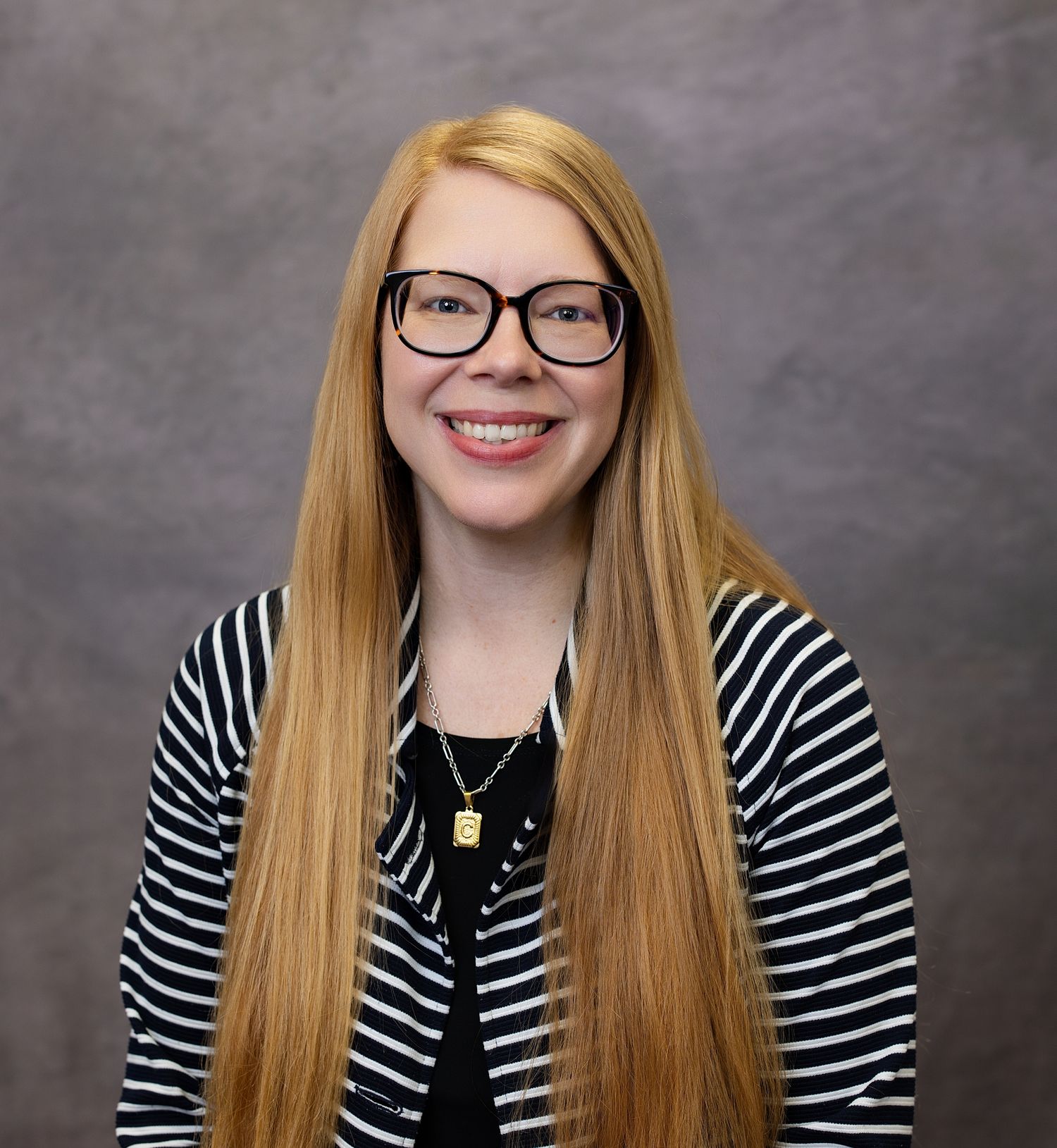 Professional portrait of someone with long blonde hair and glasses wearing a black and white striped top.