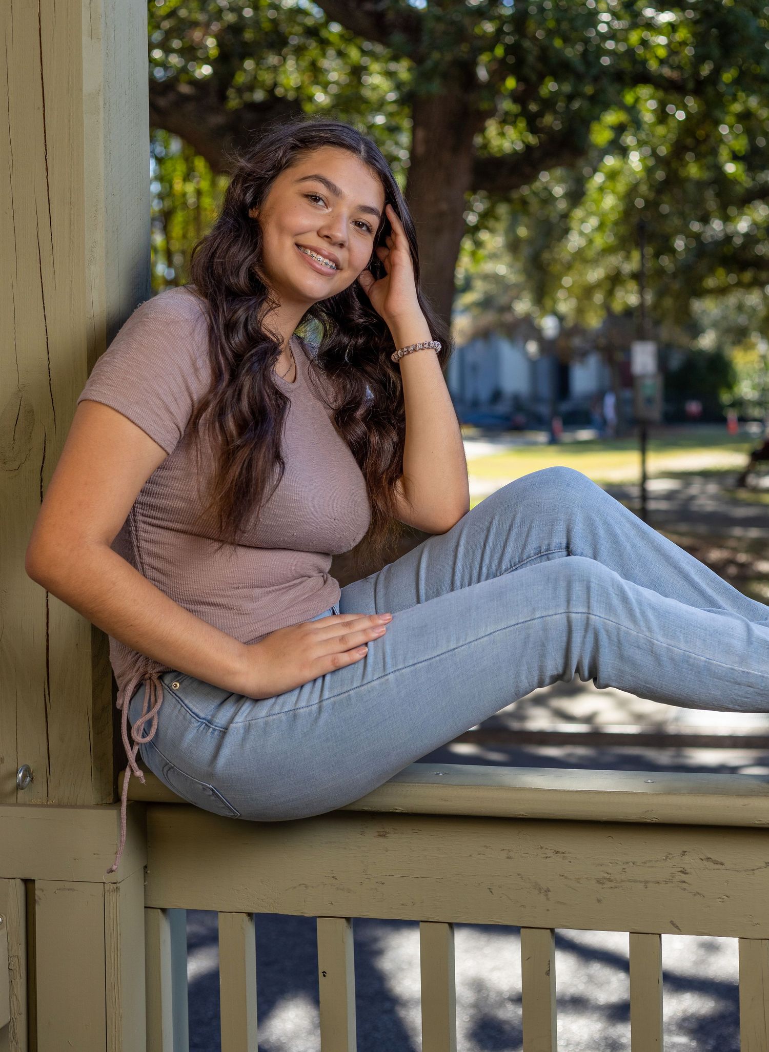 Casual outdoor portrait sitting on porch railing in natural lighting.