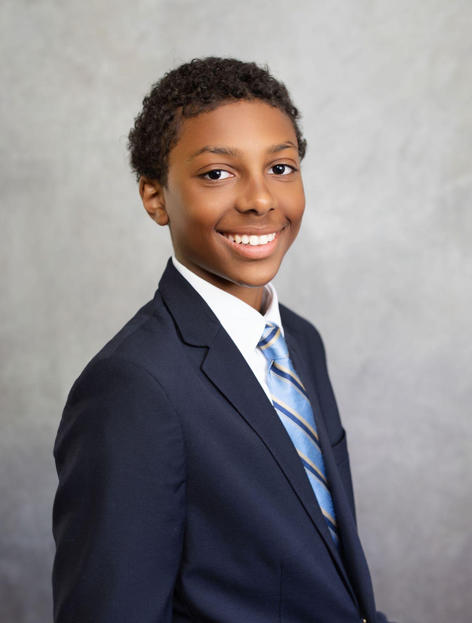 Professional studio portrait of a young person in a navy suit and striped tie against a gray backdrop.