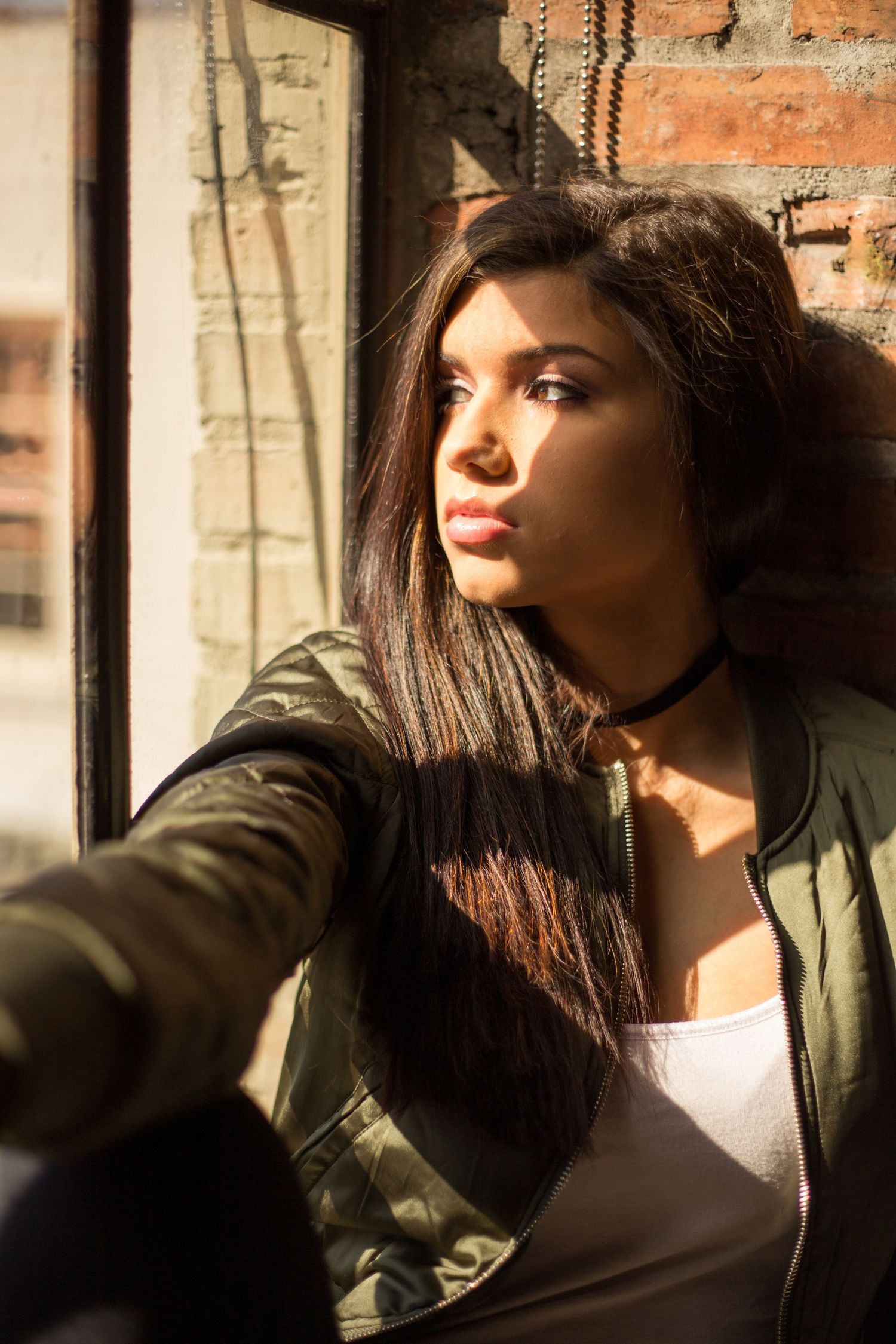 Person in olive jacket takes selfie by window with dramatic natural lighting.