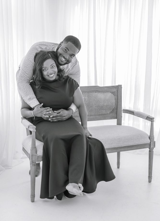 A couple shares a joyful embrace while sitting on an elegant gray upholstered French provincial style chair.