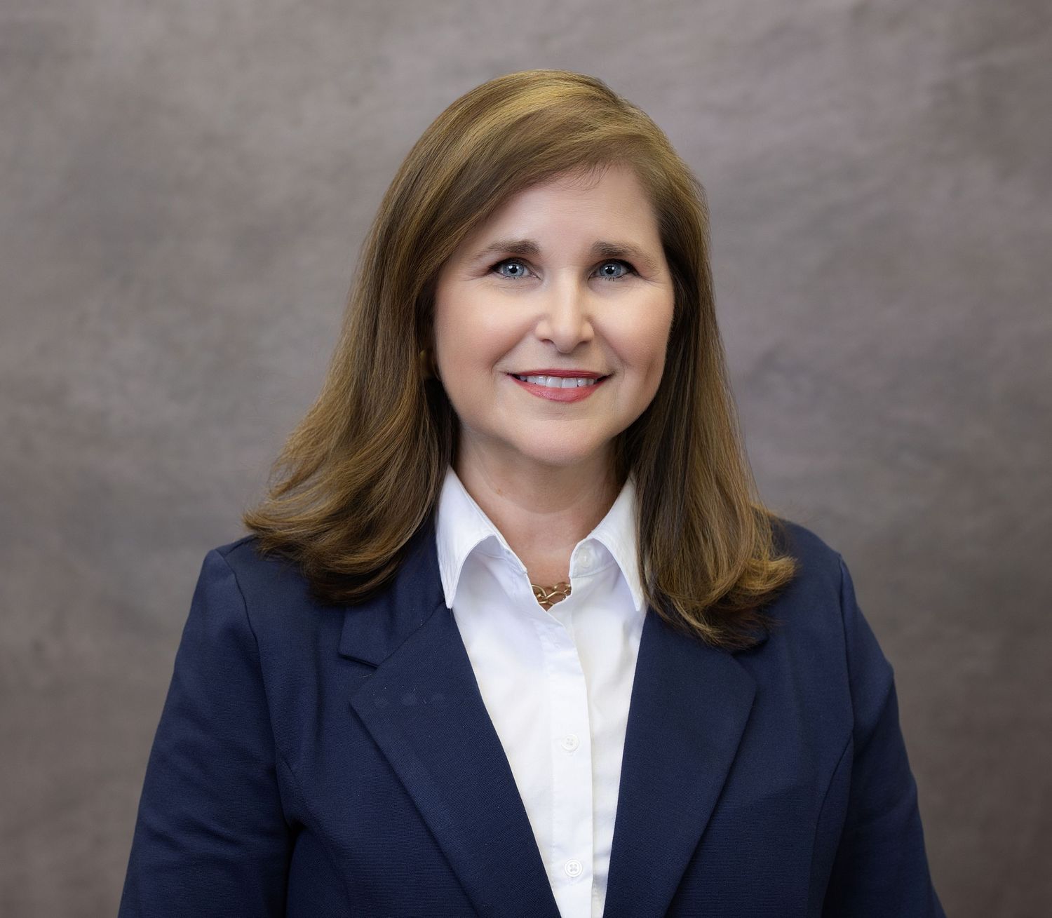 Professional headshot of a person in a navy blazer and white collared shirt against a gray background.