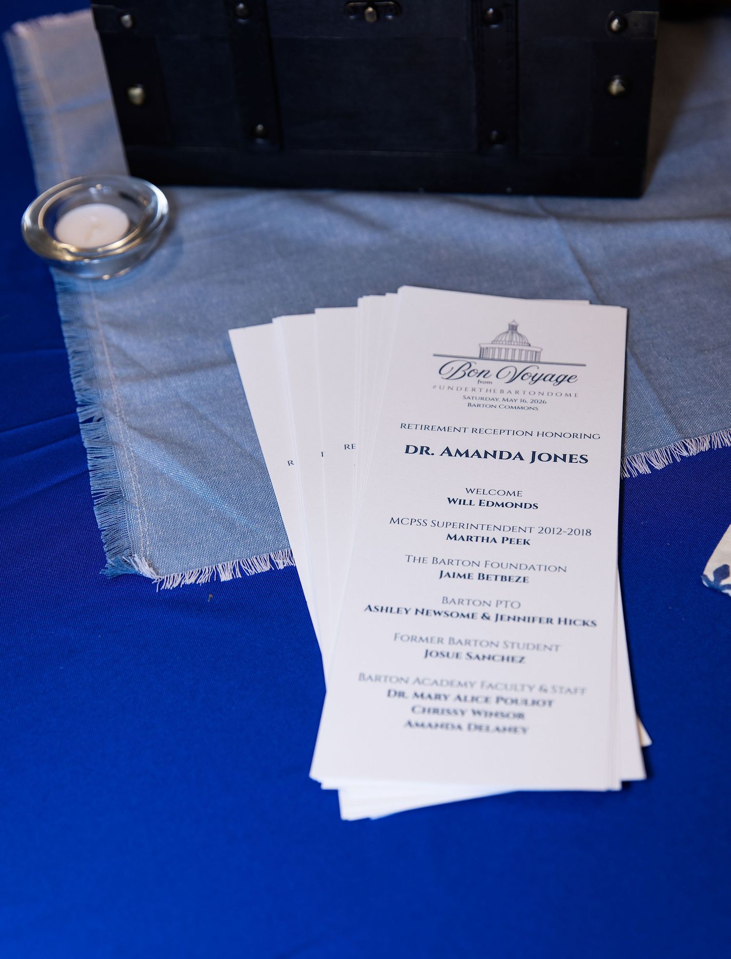 Retirement reception program for Dr. Amanda Jones displayed on a blue tablecloth at a Bon Voyage themed event.