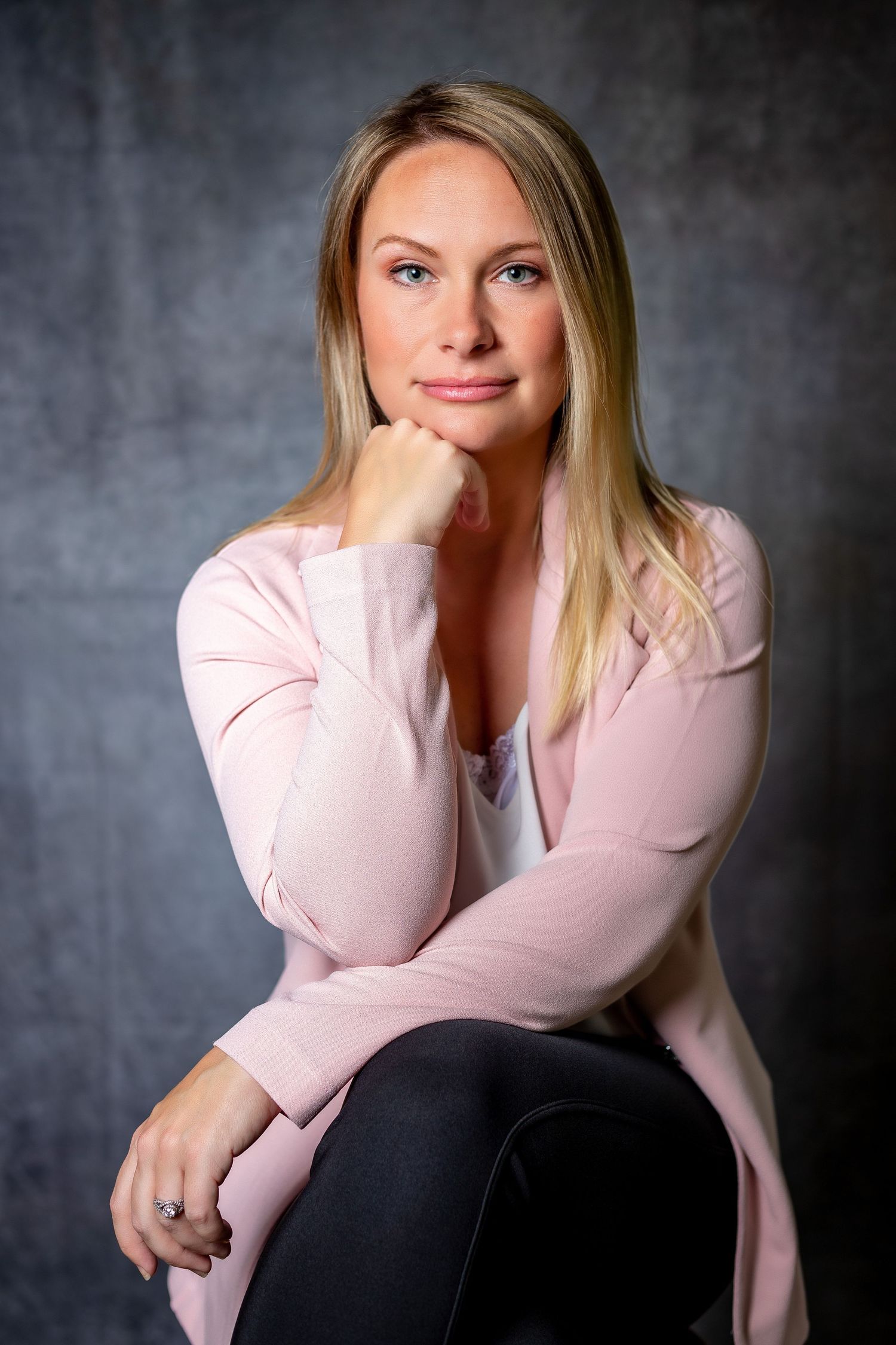Professional portrait of person in pink cardigan against dark background with contemplative pose.