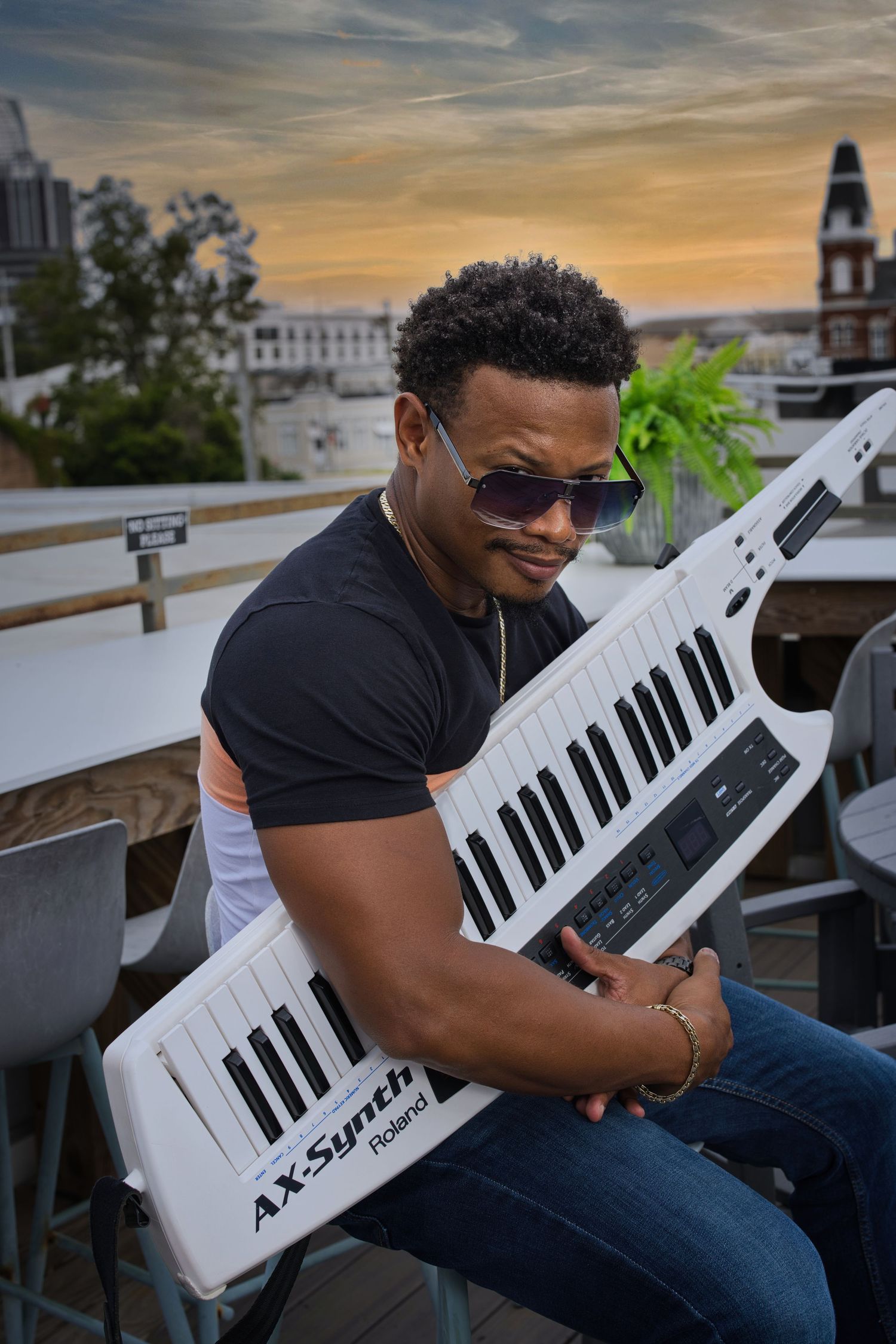 A musician plays a white keytar during sunset on an urban rooftop.