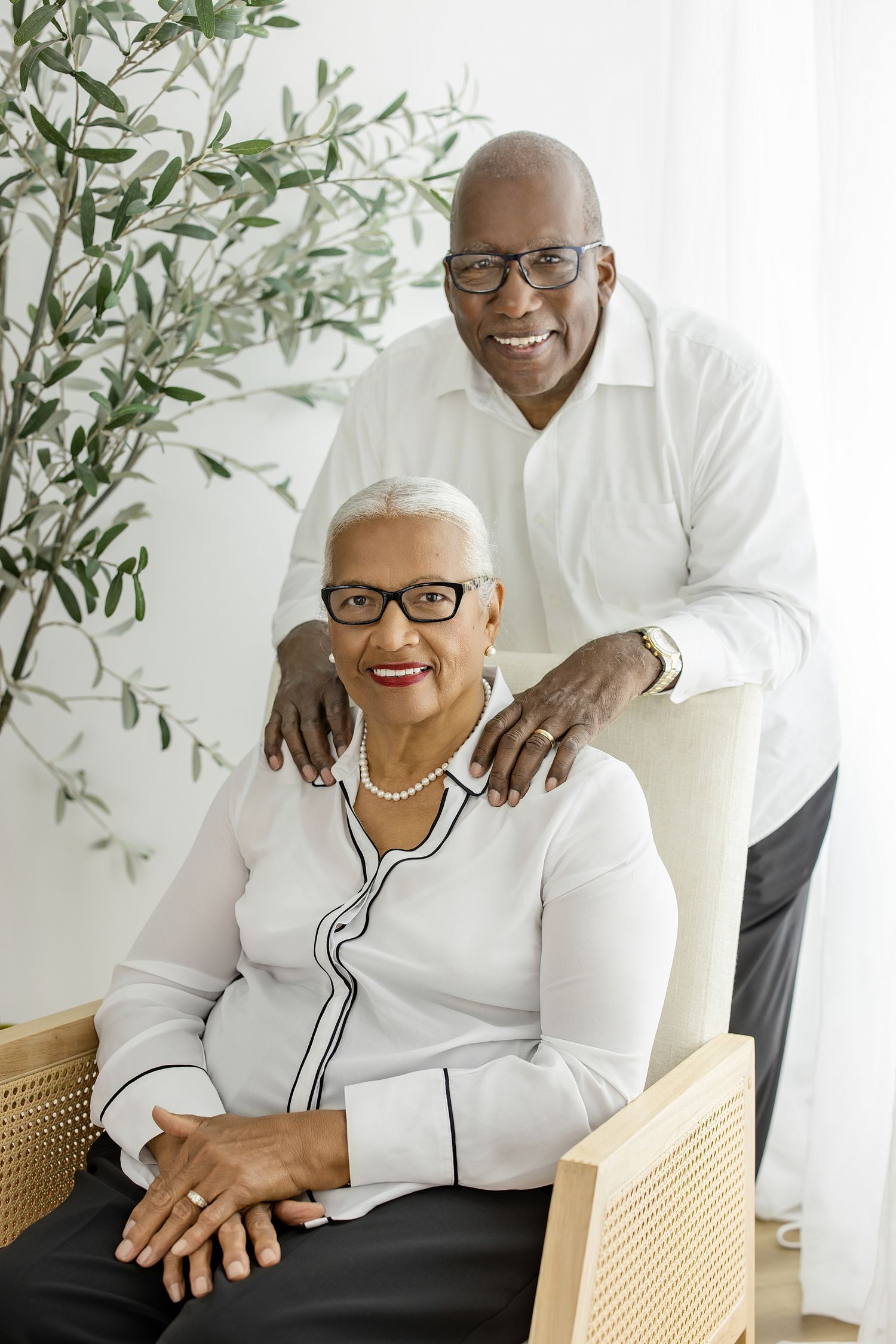 Cheerful couple in matching white outfits share warm moments while seated in a bright room with green plants.