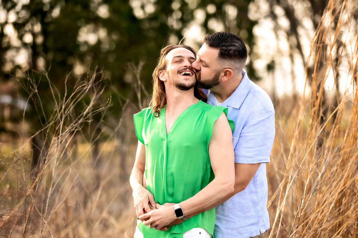 Romantic couple embraces in tall grass during golden hour sunset with vibrant green and white clothing.