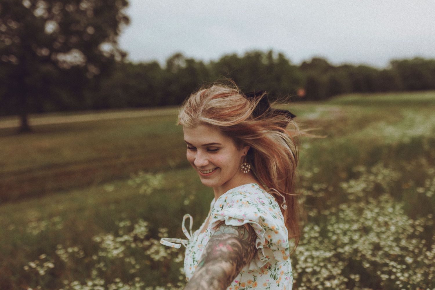 A person in a white lace dress stands joyfully in a blooming wildflower meadow on an overcast day.