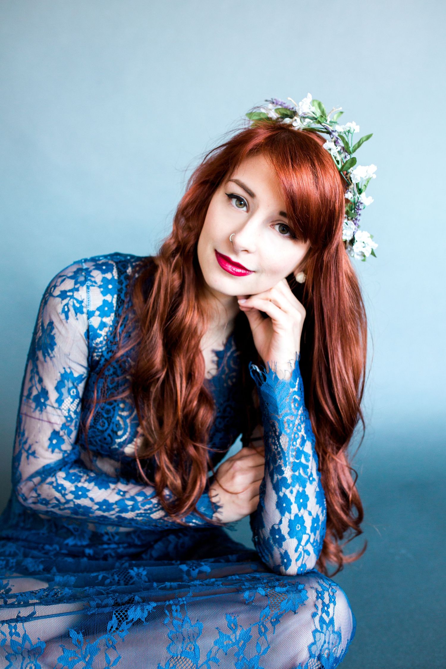 A figure in a blue lace dress lies on a light blue background with floral hair accessories.