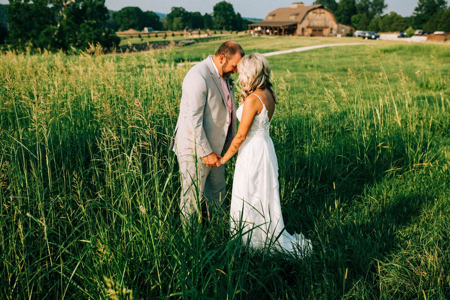 Intimate moment between newlyweds in tall summer grass field.