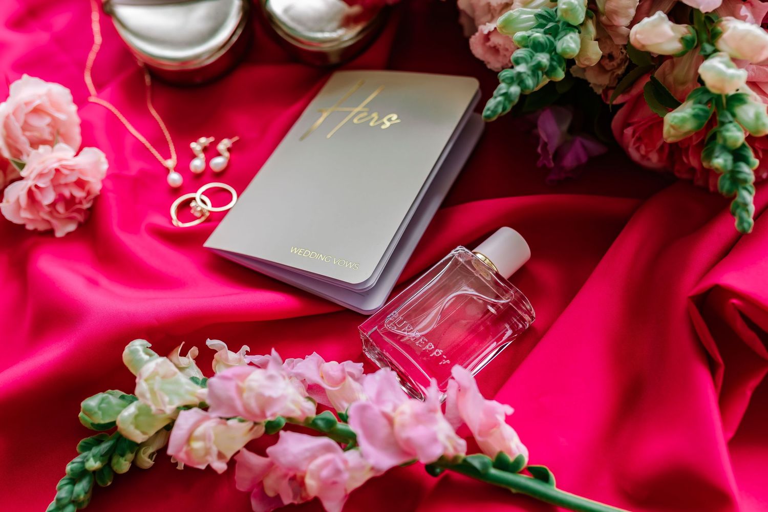 Cosmetic products and accessories styled with pink flowers and greenery against a vibrant hot pink backdrop.