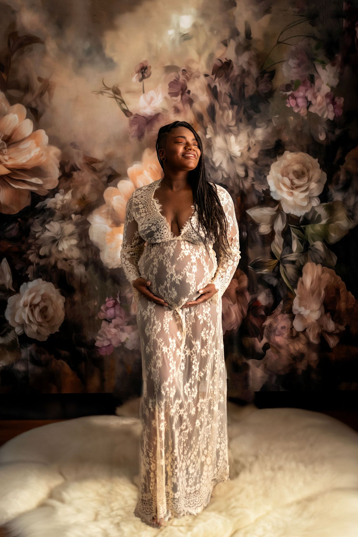 A maternity photoshoot featuring a white lace dress against a dramatic floral backdrop with moody lighting.