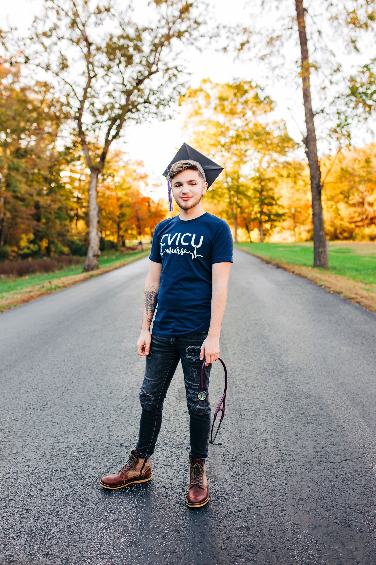 Graduate in cap and CVICU t-shirt poses on path during autumn season in Missouri..