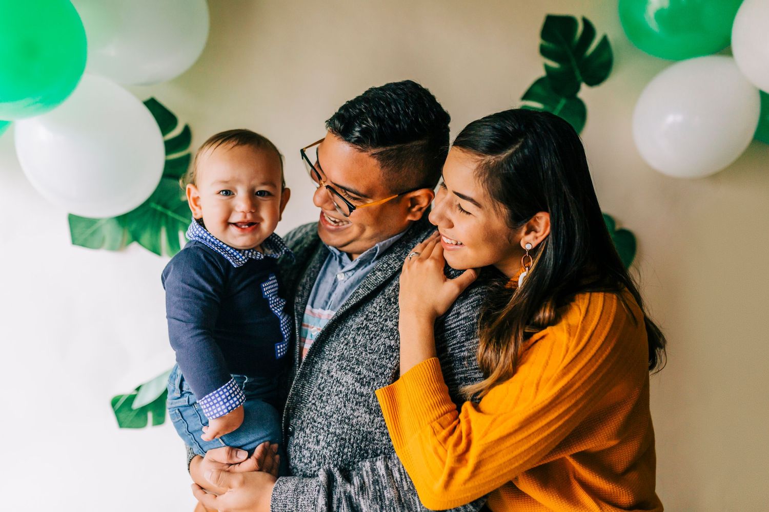 A loving family shares joyful moments together against a cream-colored wall with green and white party decorations.