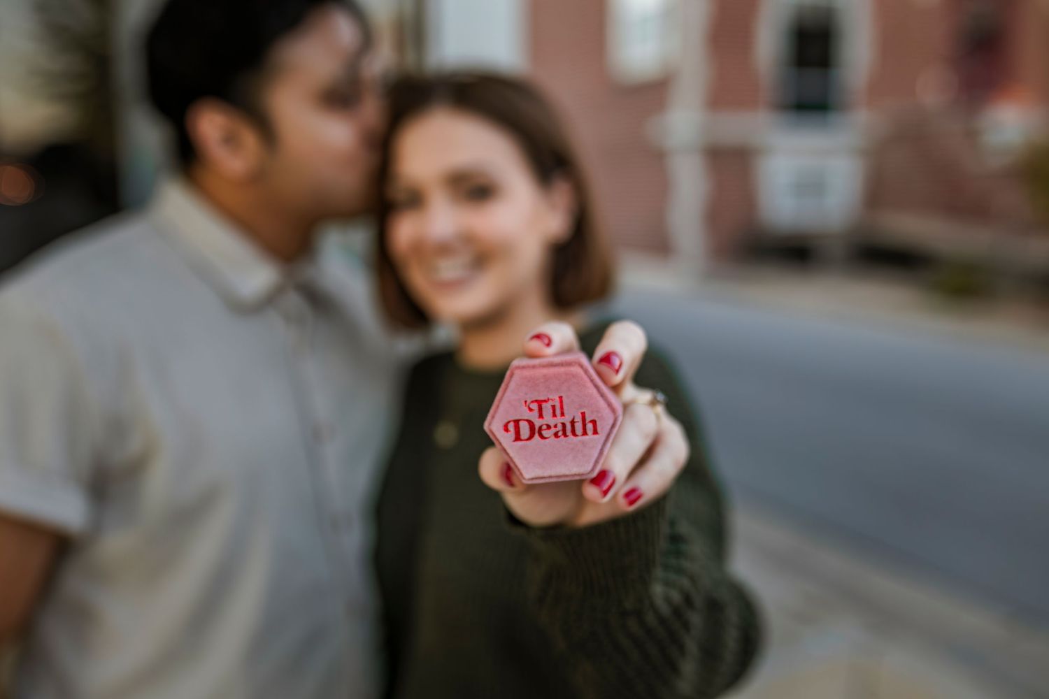 A close-up shot shows someone holding a small pink circular object in front of a blurred urban background.