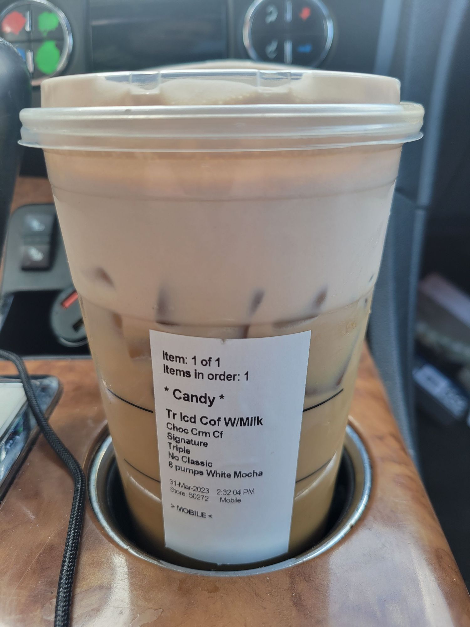 A brown boba milk tea in a clear plastic cup with a white lid sits in a car's cup holder.