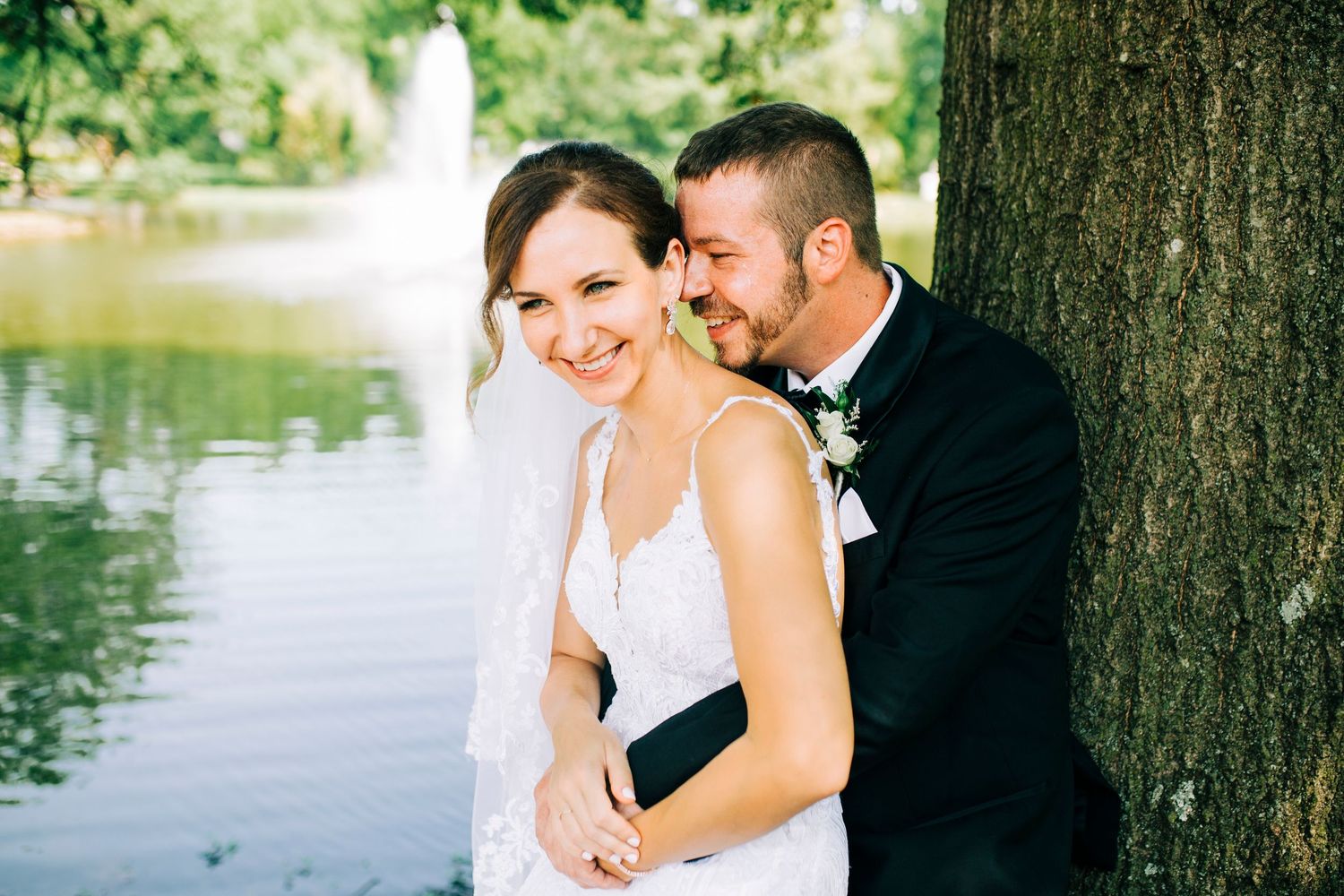 Wedding couple embracing by tree with water fountain in background in Oklahoma.