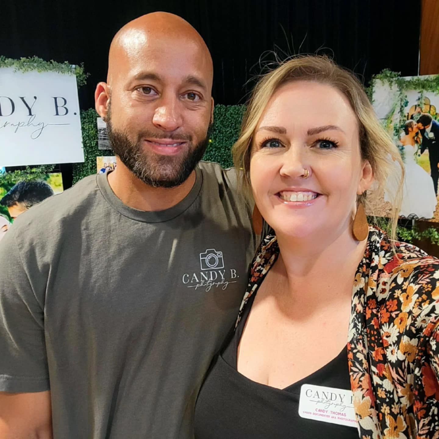 A smiling couple poses together at what appears to be an event, with decorative party decor visible in the background.