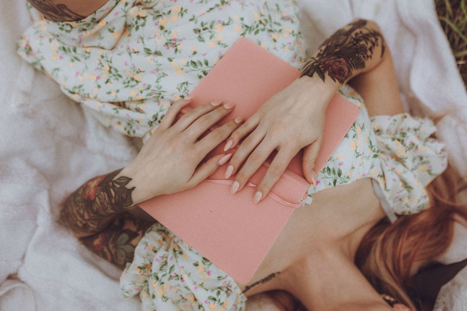 Multiple hands lay together on a pink surface against floral clothing and white fabric backdrop.