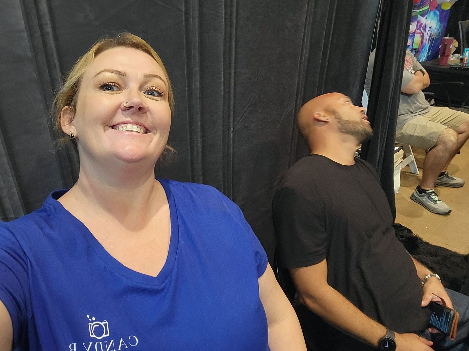 Two people sitting in a waiting area, one wearing a blue v-neck t-shirt and both appearing relaxed.