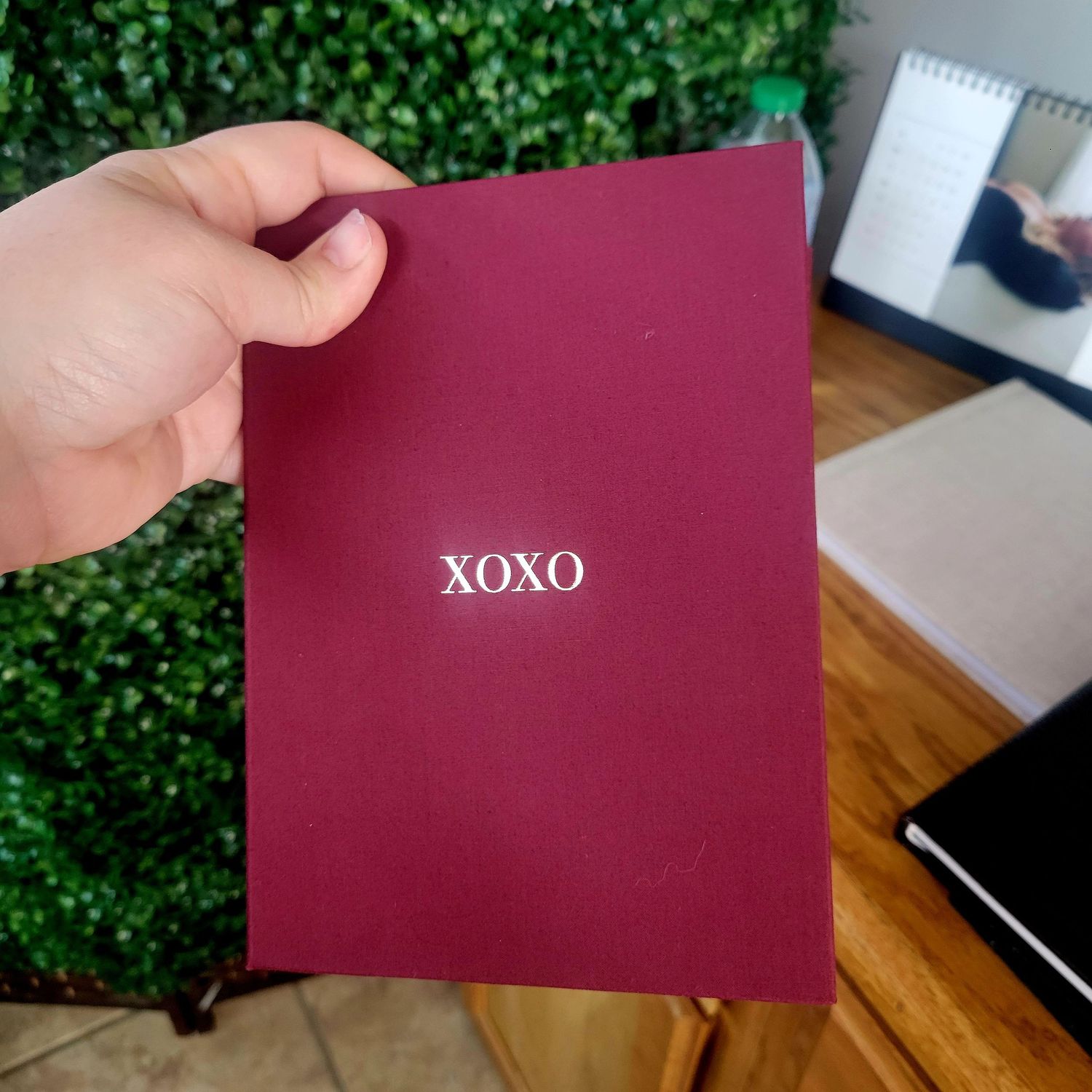A maroon red envelope rests on a wooden table with green foliage visible in the background.