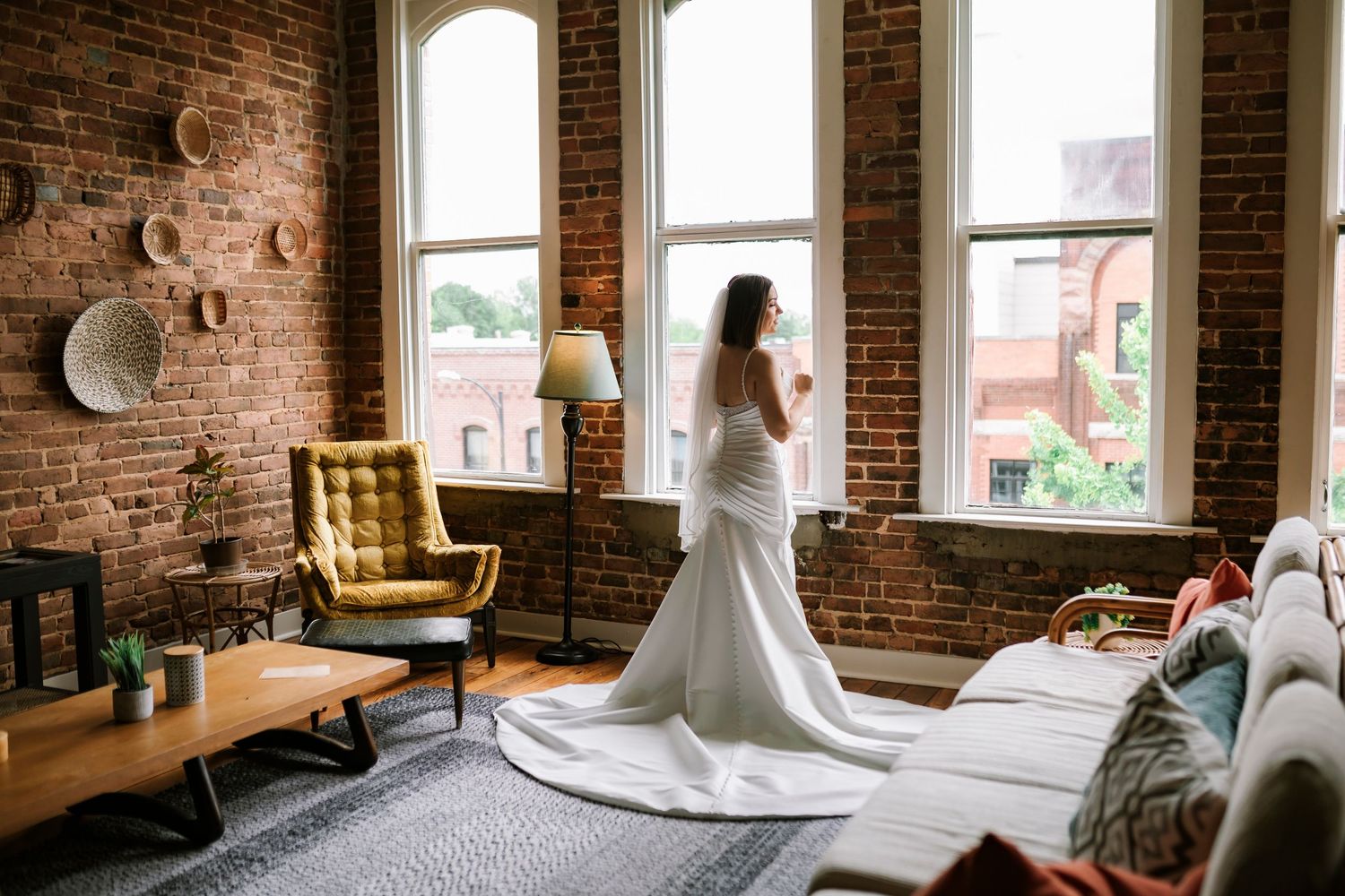 Bride in a white wedding dress standing by large windows at industrial-style airbnb on commercial street in downtown Springfield Missouri.