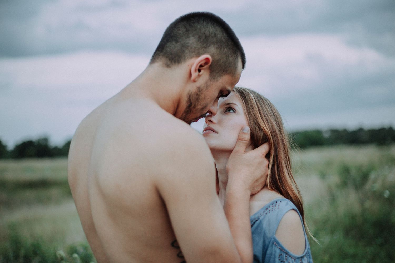 Romantic couple embraces in a misty green field during an intimate outdoor photoshoot.