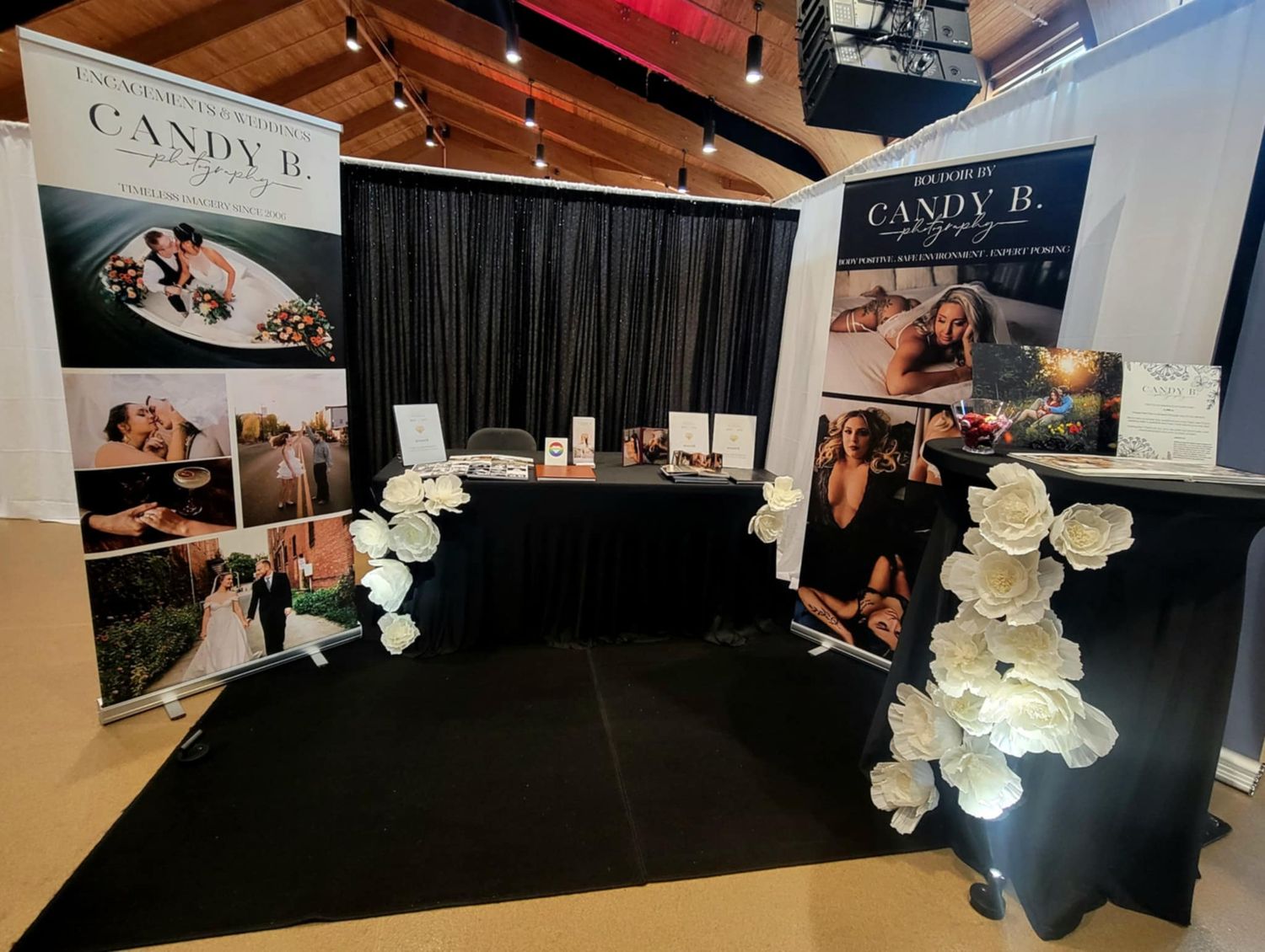 Professional photography booth setup at an event with elegant black curtains and white floral displays on display stands.