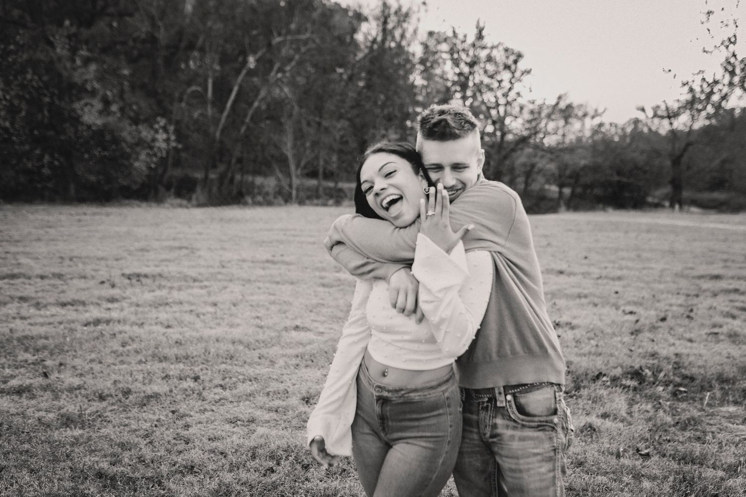 A couple laughing together in black and white while embracing in a natural outdoor setting.
