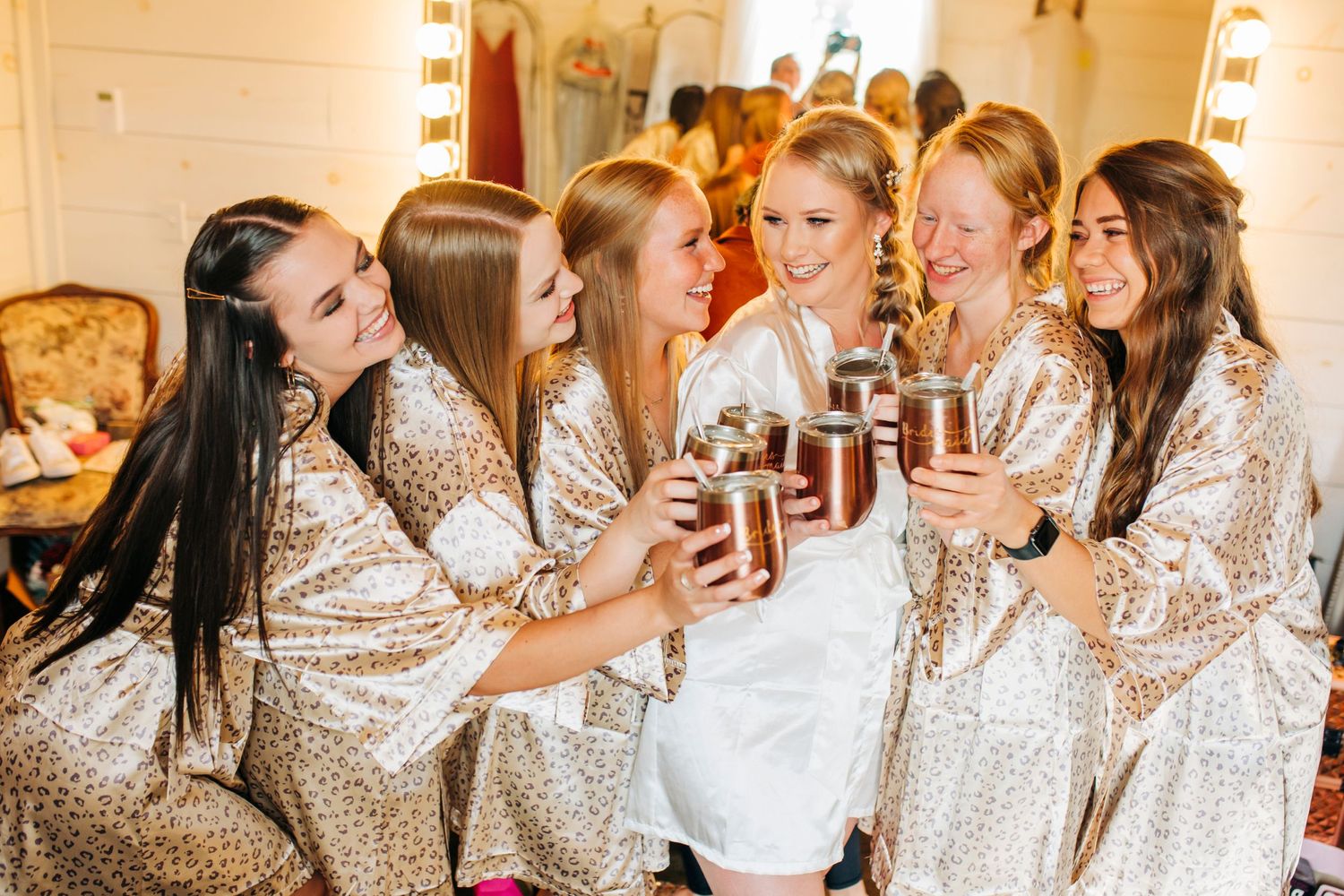 Bridesmaids in sparkly dresses toast with drinks during pre-wedding celebrations.