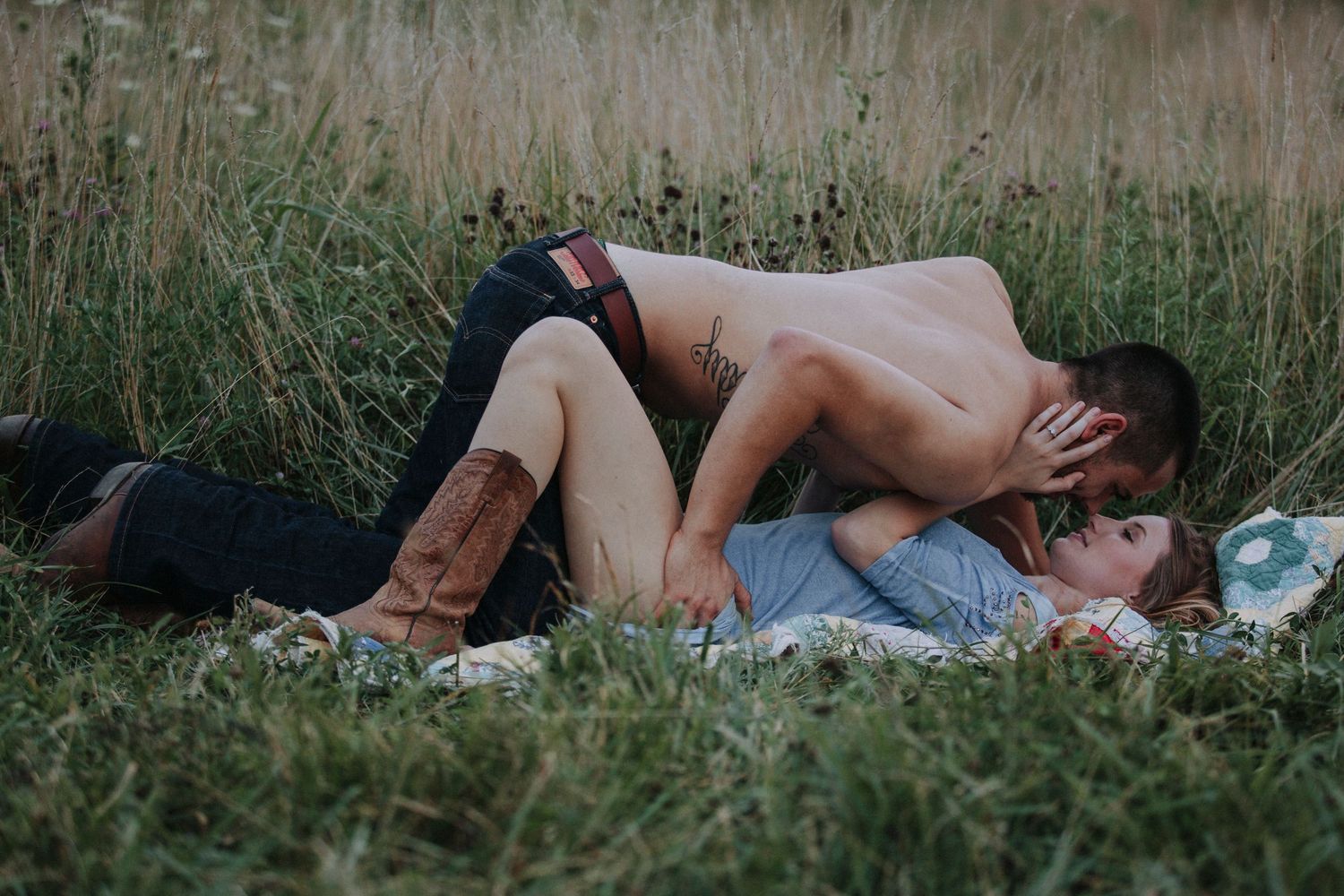 A couple lies together in tall grass during a romantic outdoor photo session.