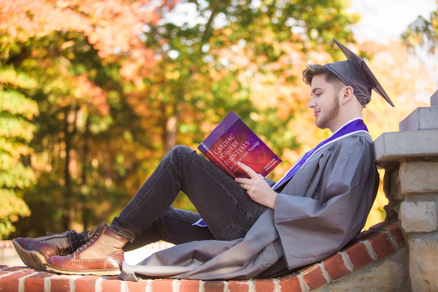 Graduate student reading in Springfield Missouri on brick wall surrounded by fall foliage.