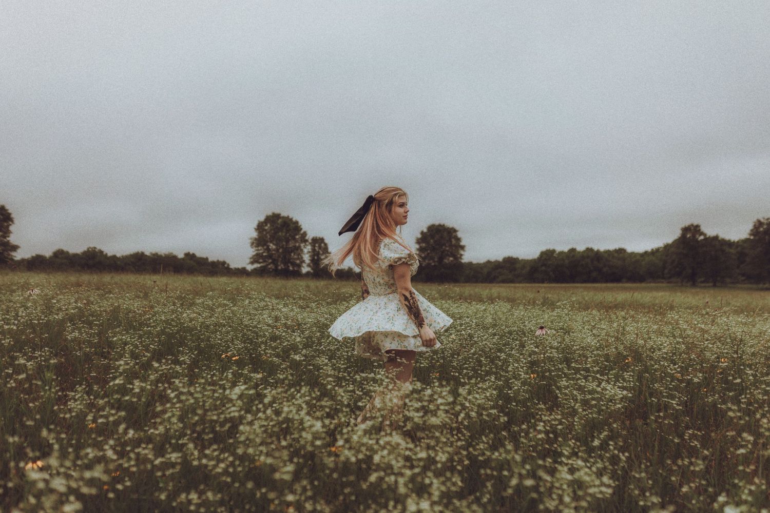 A person twirling in a white dress stands in a misty meadow at dusk, with their hair flowing in motion.